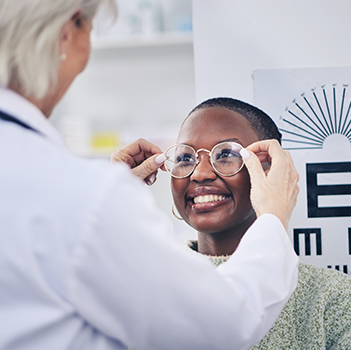 Optometrist fits glasses on smiling woman